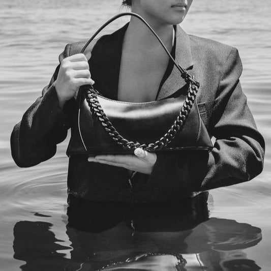 Black and white shot of bag in arms of model wearing suit jack standing in water